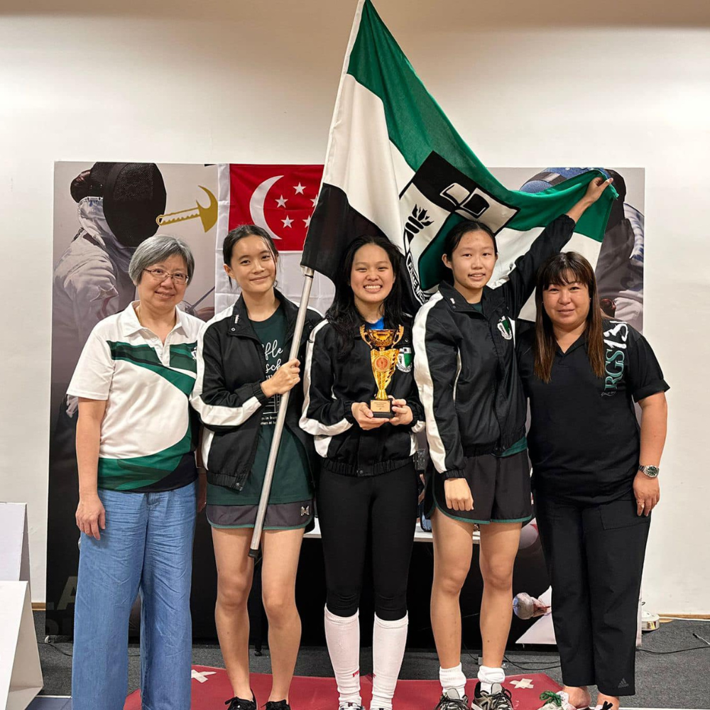 Five people pose with a trophy and green-black-white flag in front of a Singapore flag backdrop.